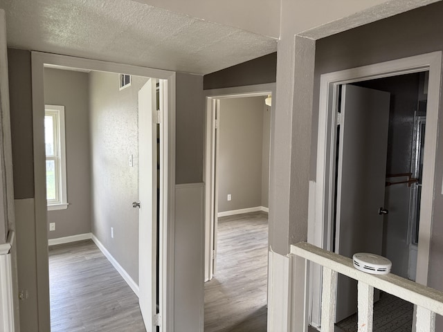 hallway featuring a textured ceiling, wood finished floors, baseboards, and visible vents