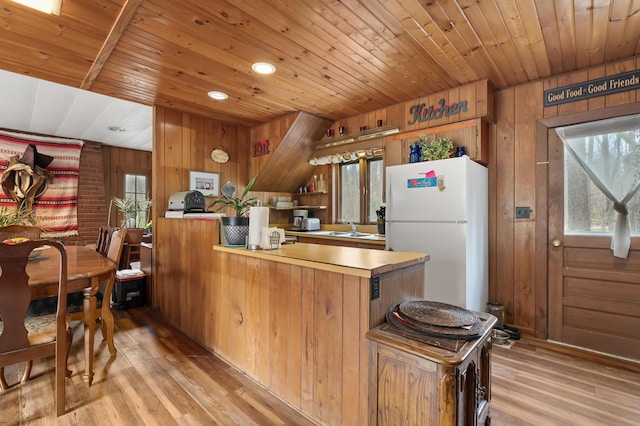 kitchen with a peninsula, wooden ceiling, freestanding refrigerator, and wood walls