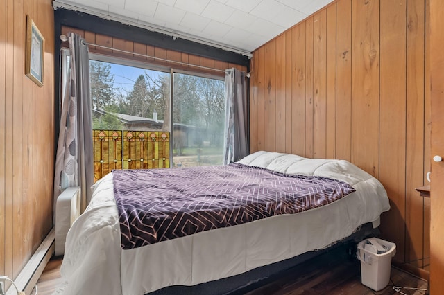 bedroom featuring wood walls, baseboard heating, access to exterior, and wood finished floors