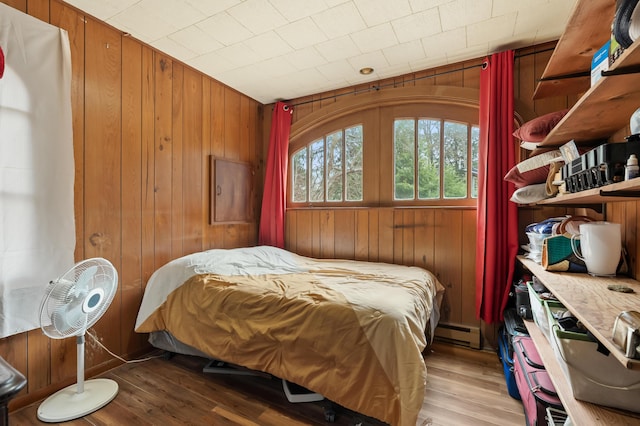 bedroom with baseboard heating, wood finished floors, and wood walls