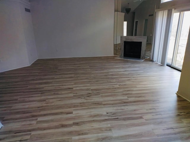 unfurnished living room with a fireplace with raised hearth, a high ceiling, visible vents, and wood finished floors