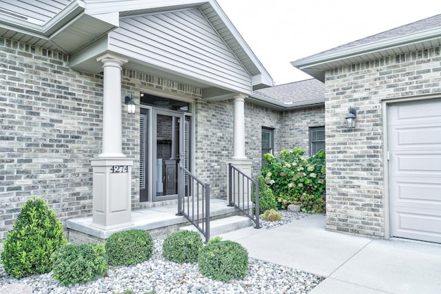 view of exterior entry featuring brick siding, a shingled roof, and a garage