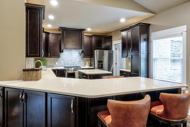 kitchen featuring tasteful backsplash, light countertops, premium range hood, a peninsula, and high end appliances