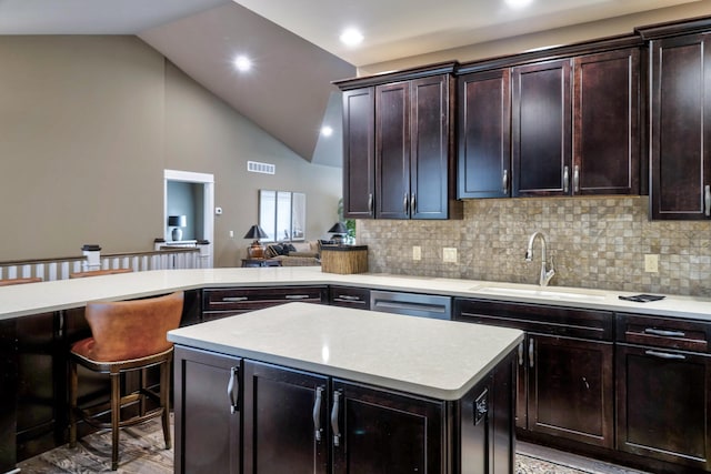 kitchen featuring light countertops, a kitchen island, visible vents, decorative backsplash, and a sink