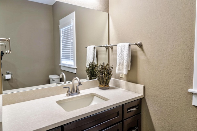 half bath featuring a textured wall, vanity, and toilet