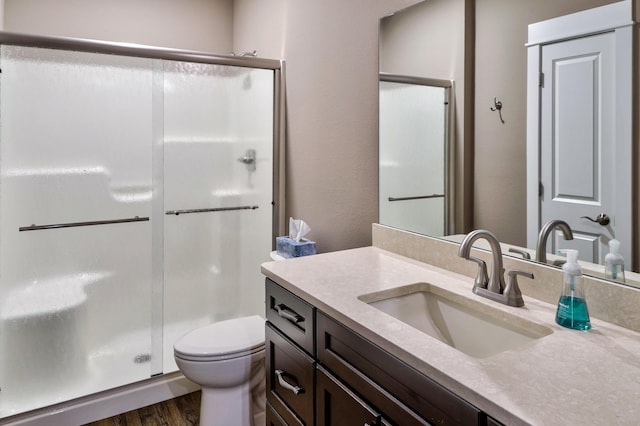 bathroom with toilet, vanity, a stall shower, and wood finished floors