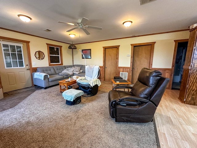 living area featuring wainscoting, visible vents, a ceiling fan, and crown molding