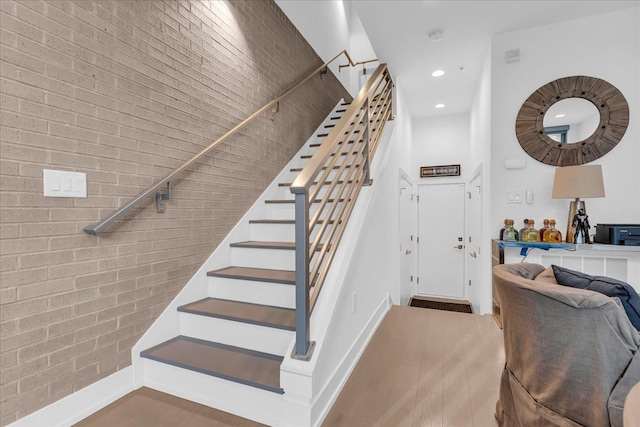 stairway with brick wall, baseboards, recessed lighting, and wood finished floors
