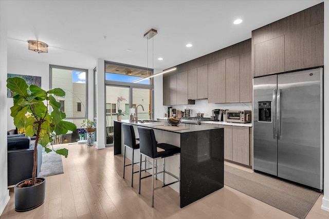 kitchen featuring stainless steel fridge with ice dispenser, an island with sink, a kitchen bar, a wall of windows, and a sink