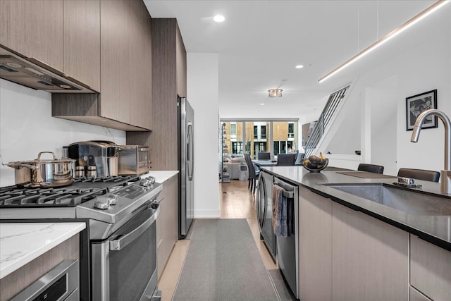 kitchen featuring modern cabinets, appliances with stainless steel finishes, light stone counters, a sink, and open floor plan
