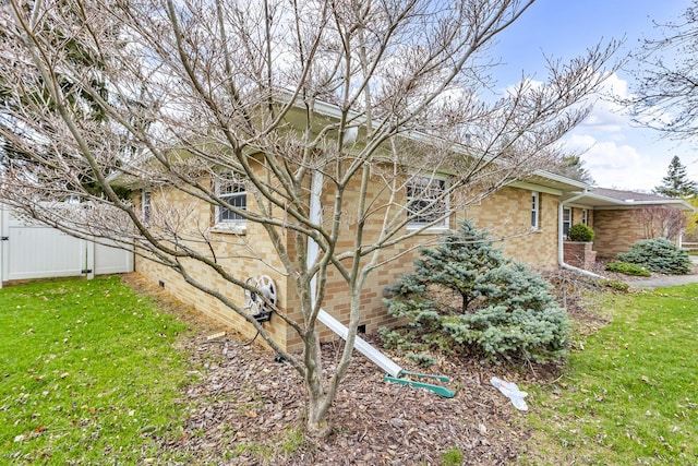 view of home's exterior with a yard, brick siding, and fence