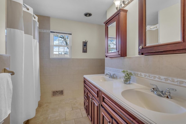 full bathroom with visible vents, tile walls, a sink, and wainscoting