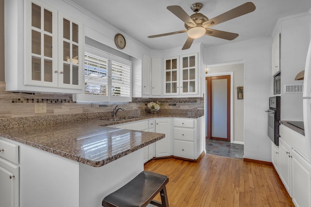 kitchen with a sink, light wood-style flooring, oven, and white cabinetry