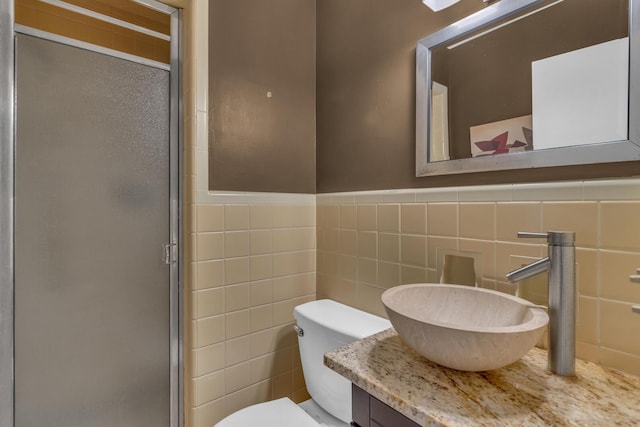 bathroom featuring a shower stall, vanity, toilet, wainscoting, and tile walls