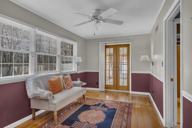 living area with wood finished floors, a ceiling fan, plenty of natural light, and a wainscoted wall