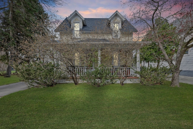 view of front facade featuring roof with shingles, a lawn, and covered porch