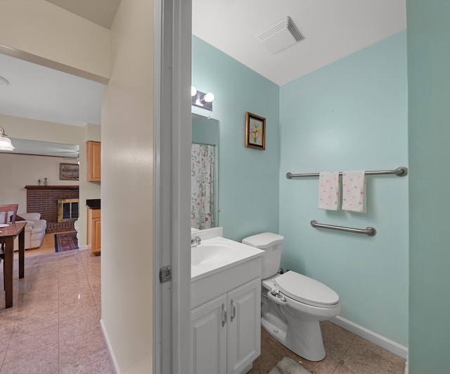 bathroom with vanity, visible vents, toilet, a brick fireplace, and tile patterned floors