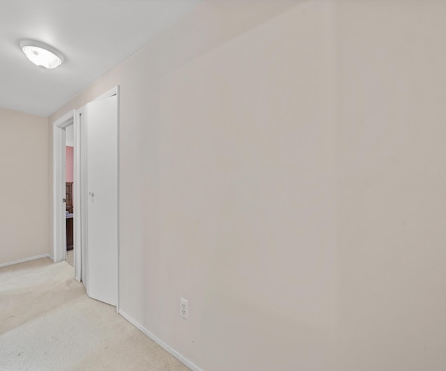 hall featuring baseboards and light colored carpet