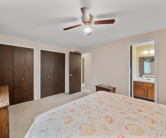 bedroom featuring carpet flooring, ensuite bath, two closets, a ceiling fan, and a sink