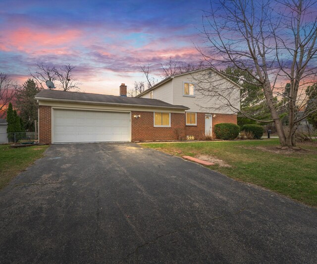 view of front of house featuring a chimney, aphalt driveway, brick siding, a garage, and a yard