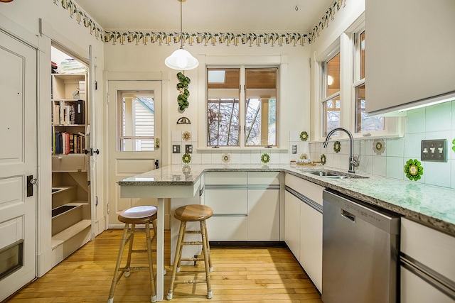 kitchen featuring stainless steel dishwasher, tasteful backsplash, a sink, light wood-style floors, and pendant lighting
