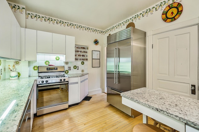 kitchen featuring white cabinets, tasteful backsplash, light wood-style floors, light stone countertops, and appliances with stainless steel finishes