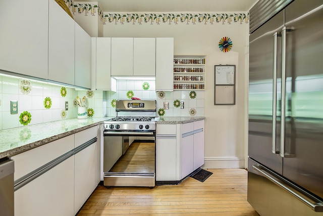 kitchen with backsplash, white cabinetry, stainless steel appliances, and light wood-style floors