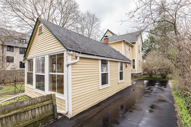 view of side of home featuring roof with shingles and fence