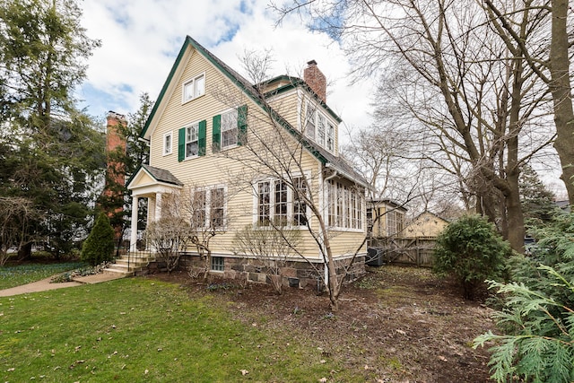 view of side of property with fence, a lawn, a chimney, and central AC