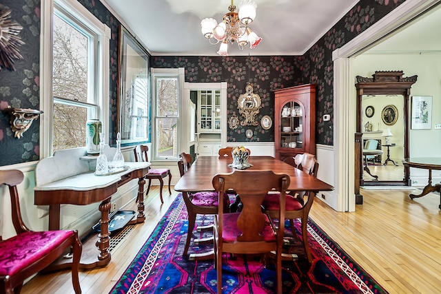 dining space with wallpapered walls, a wainscoted wall, wood-type flooring, crown molding, and a notable chandelier