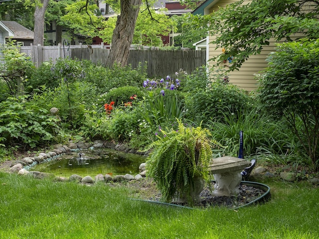 view of yard featuring fence and a garden pond