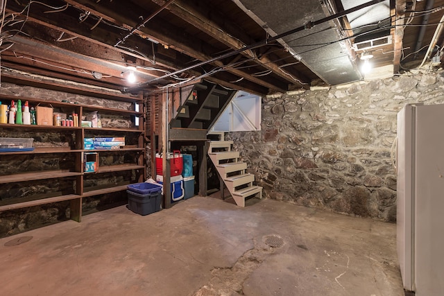 unfinished basement with stairway and freestanding refrigerator