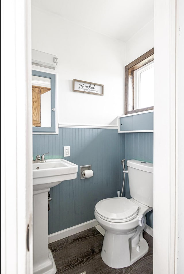 half bath featuring a wainscoted wall, baseboards, toilet, and wood finished floors