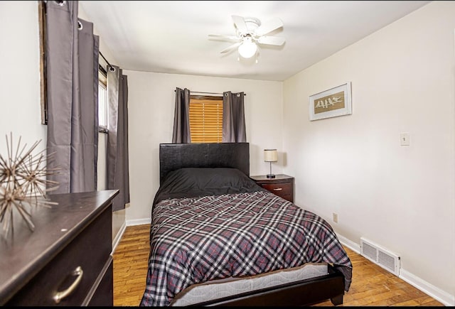bedroom with ceiling fan, visible vents, baseboards, and wood finished floors