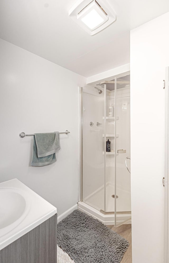 full bath featuring a shower stall, wood finished floors, vanity, and baseboards
