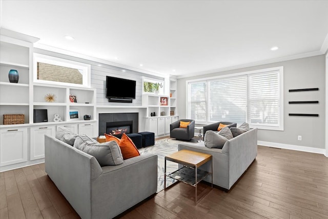 living room featuring crown molding, built in features, baseboards, a glass covered fireplace, and dark wood-type flooring
