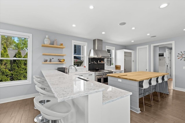 kitchen featuring butcher block counters, a kitchen breakfast bar, wall chimney range hood, high quality appliances, and a sink