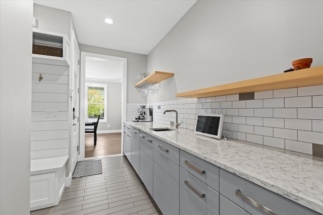 kitchen with open shelves, gray cabinetry, decorative backsplash, and a sink