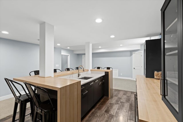 kitchen featuring baseboards, a sink, recessed lighting, and a kitchen bar