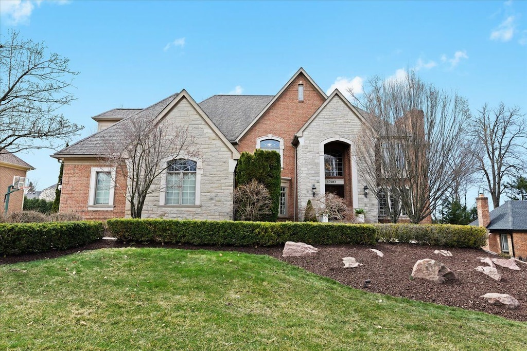french country inspired facade featuring brick siding, stone siding, and a front yard