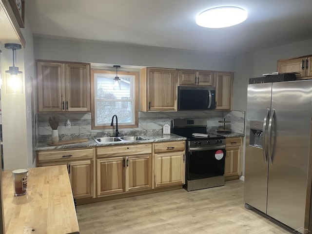 kitchen featuring stainless steel appliances, light wood-style floors, a sink, and backsplash