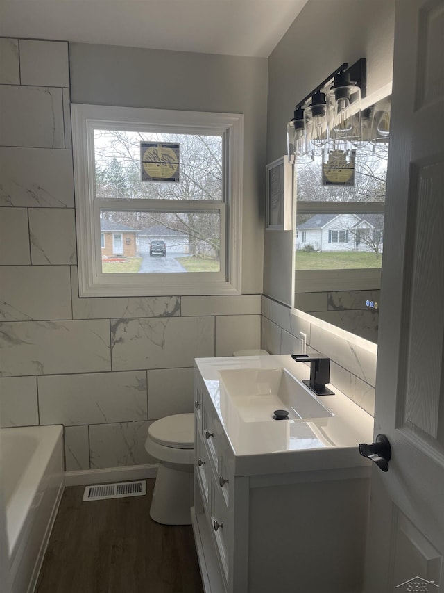 full bathroom featuring vanity, visible vents, toilet, wood finished floors, and a bathtub