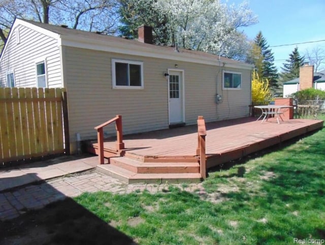 rear view of house with a chimney, a wooden deck, fence, and a lawn