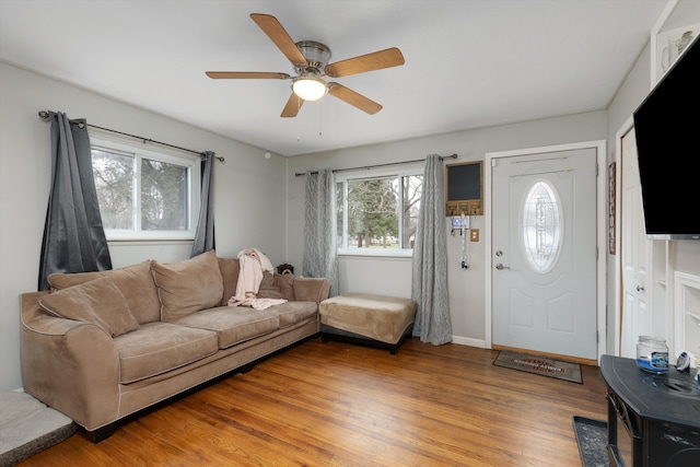 living room featuring baseboards, a ceiling fan, and light wood finished floors
