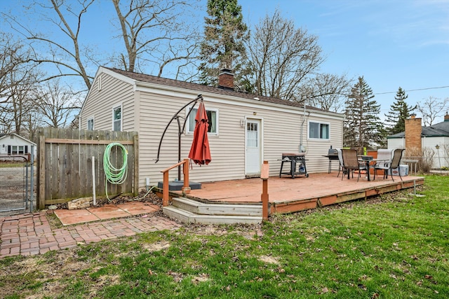 back of house with a deck, a chimney, fence, and a lawn