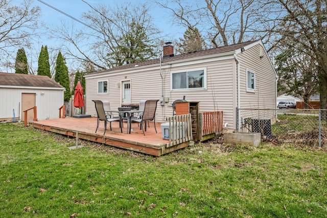 back of property with an outdoor structure, a chimney, a wooden deck, a yard, and fence
