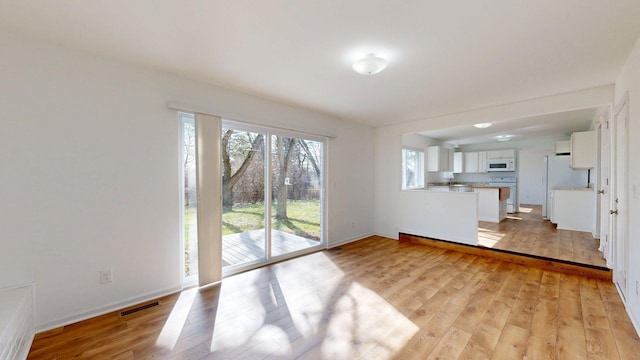 unfurnished living room with light wood-style floors, baseboards, and visible vents
