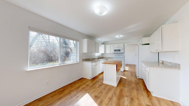 kitchen featuring white appliances, white cabinetry, a center island, a sink, and light wood finished floors