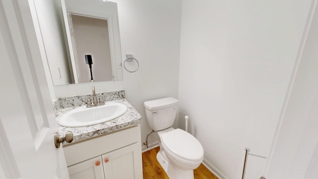 bathroom with toilet, vanity, wood finished floors, and baseboards