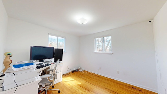 office space featuring plenty of natural light, light wood finished floors, visible vents, and baseboards